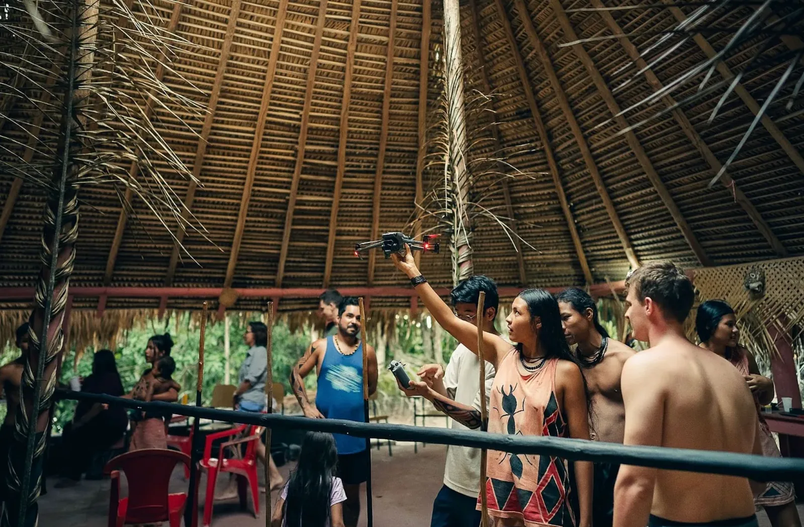 Indigenous community gathering inside a maloca, launching a drone